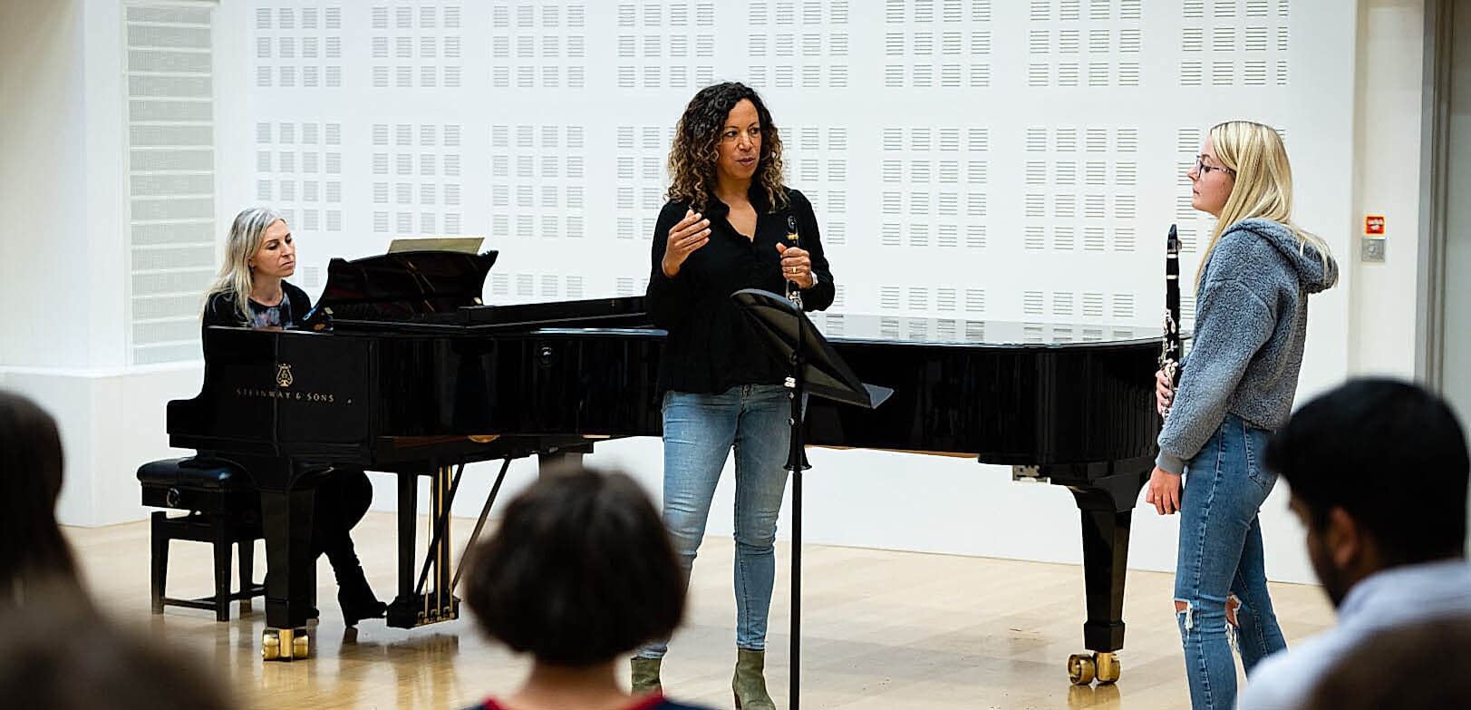 A student and tutor stand talking in front of a music stand holding clarinets as part of a class. 