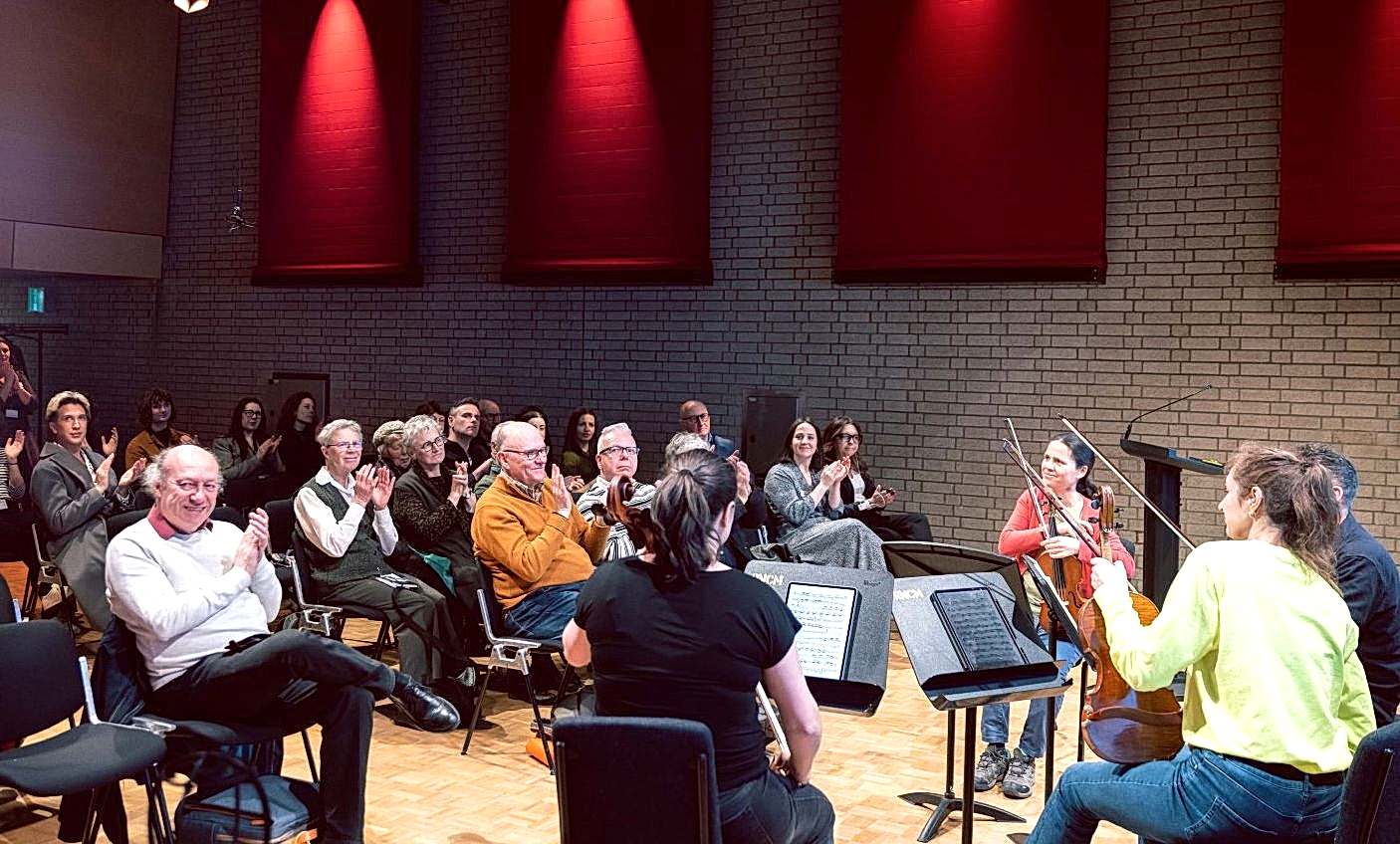 Photo of a small audience applauding a string quartet in a small concert hall.