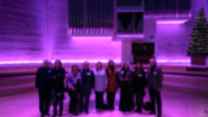 A group of nine people stand on the stage of an RNCM theatre under purple lights. 