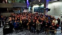 A large group of people stand on the RNCM concourse holding glasses and smiling. 